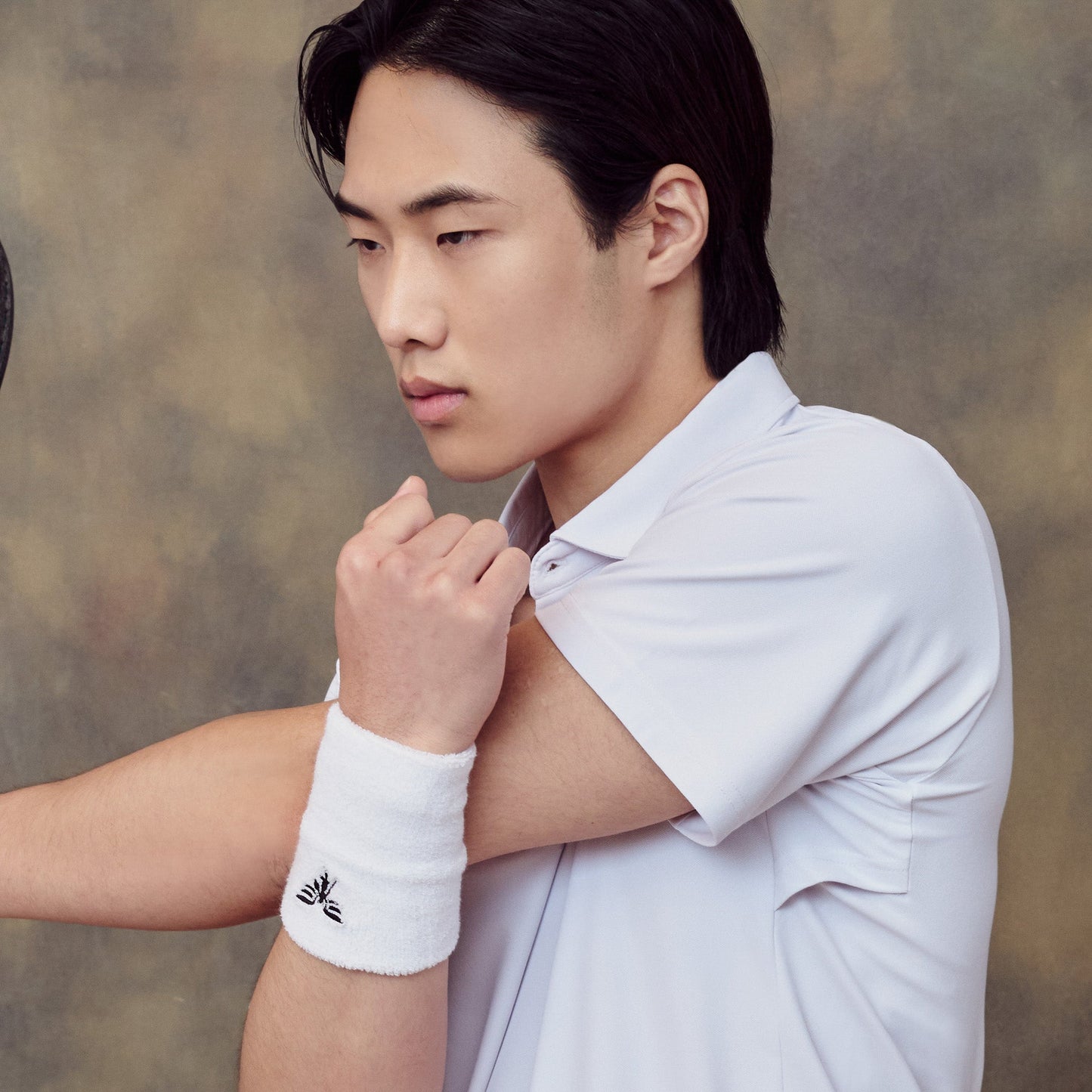 Man wearing a white shirt and wristband against a neutral background