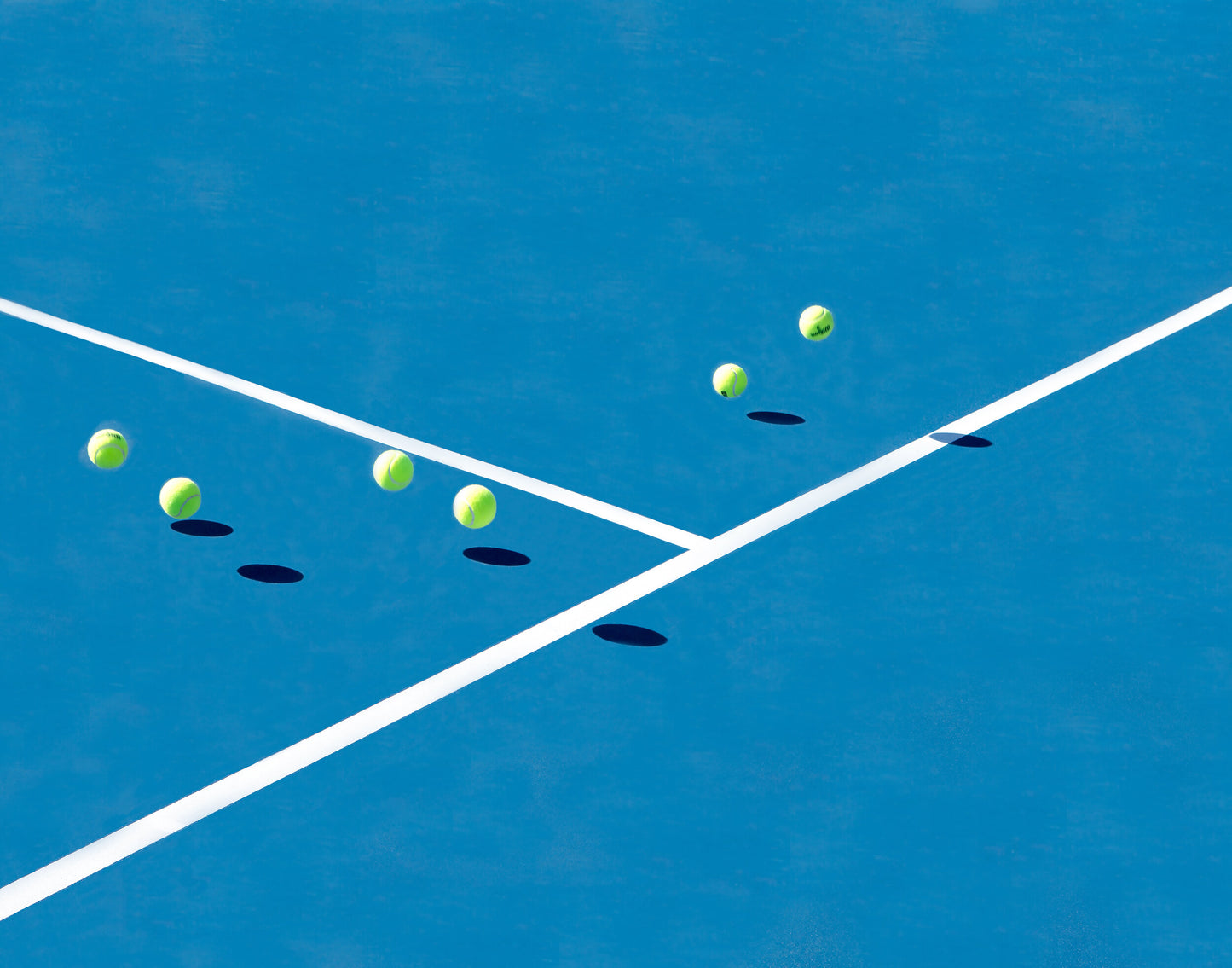 Yellow tennis balls bouncing on a blue tennis court. 