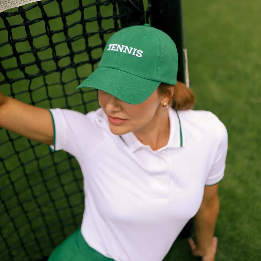 Lady wearing a green tennis hat on a tennis court. 