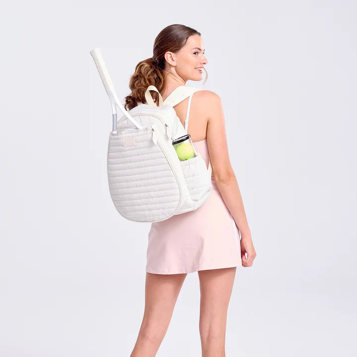 Woman wearing a white backpack with a tennis racket and ball on a light gray background