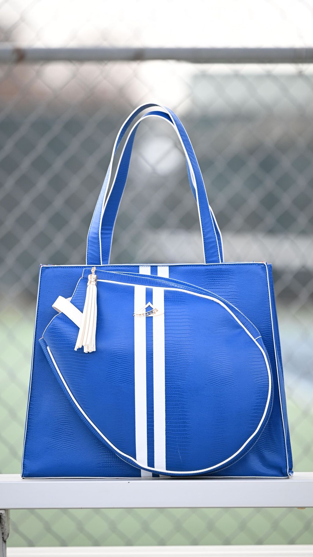 Blue tote bag with white stripes and tassels on a metal surface.