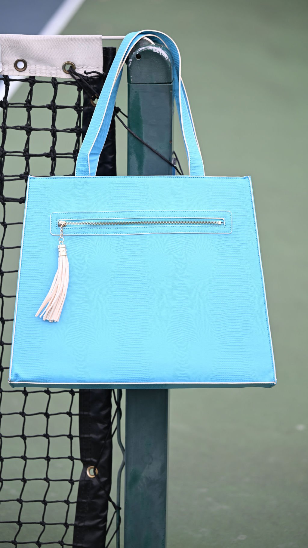 Blue handbag with a tassel hanging on a tennis net